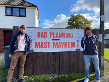 James Daly MP and Cllr Liam James Dean stand in front of the planned mast location with a "Bad Planning Mast Mayhem" sign